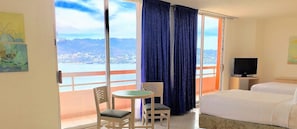 Een hotelkamer met balkon, een bed, een televisie en een kleine tafel met stoelen.