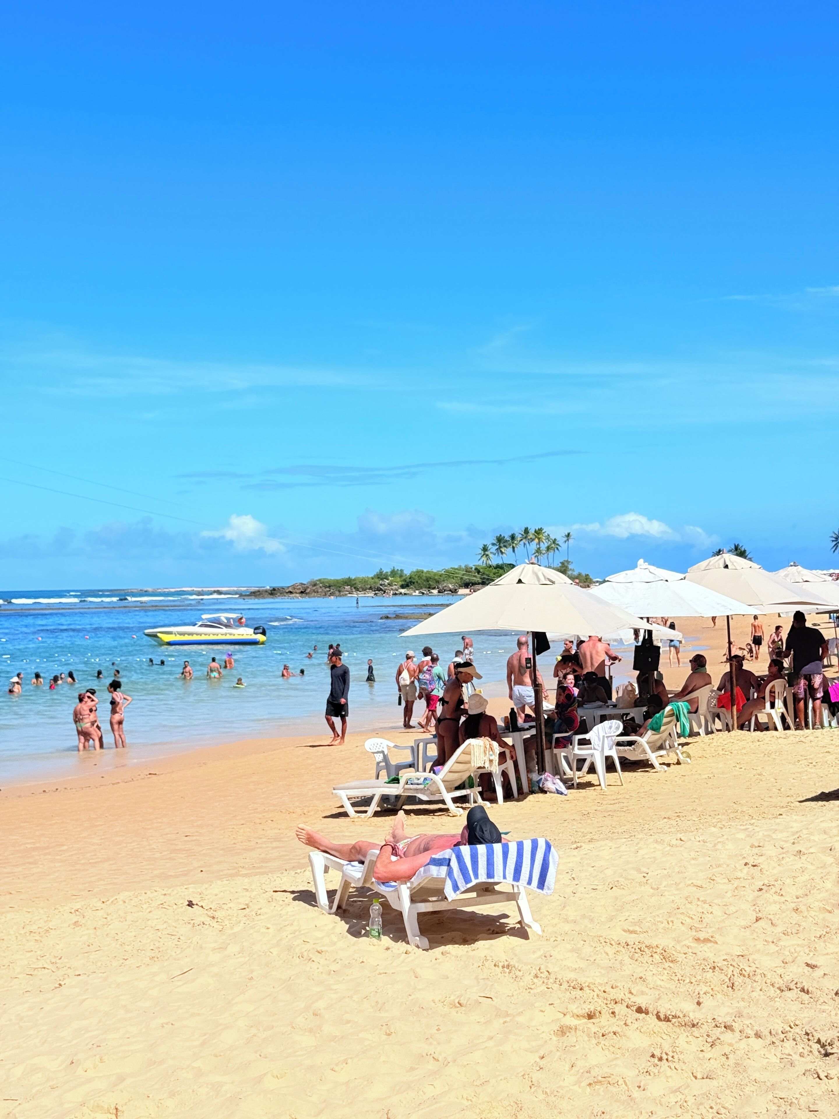 A beach with people swimming and sunbathing, umbrellas, and lounge chairs.