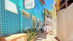 Ein schmaler Gang mit einem blauen Gebäude auf der linken Seite, einer hölzernen Bank und einem Schild mit der Aufschrift 'Vila do Motro'.