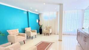 Ein modernes Wohnzimmer mit einer türkisfarbenen Akzentwand, beigen Sofas, einem Couchtisch und einem großen Fenster mit durchscheinenden Vorhängen.