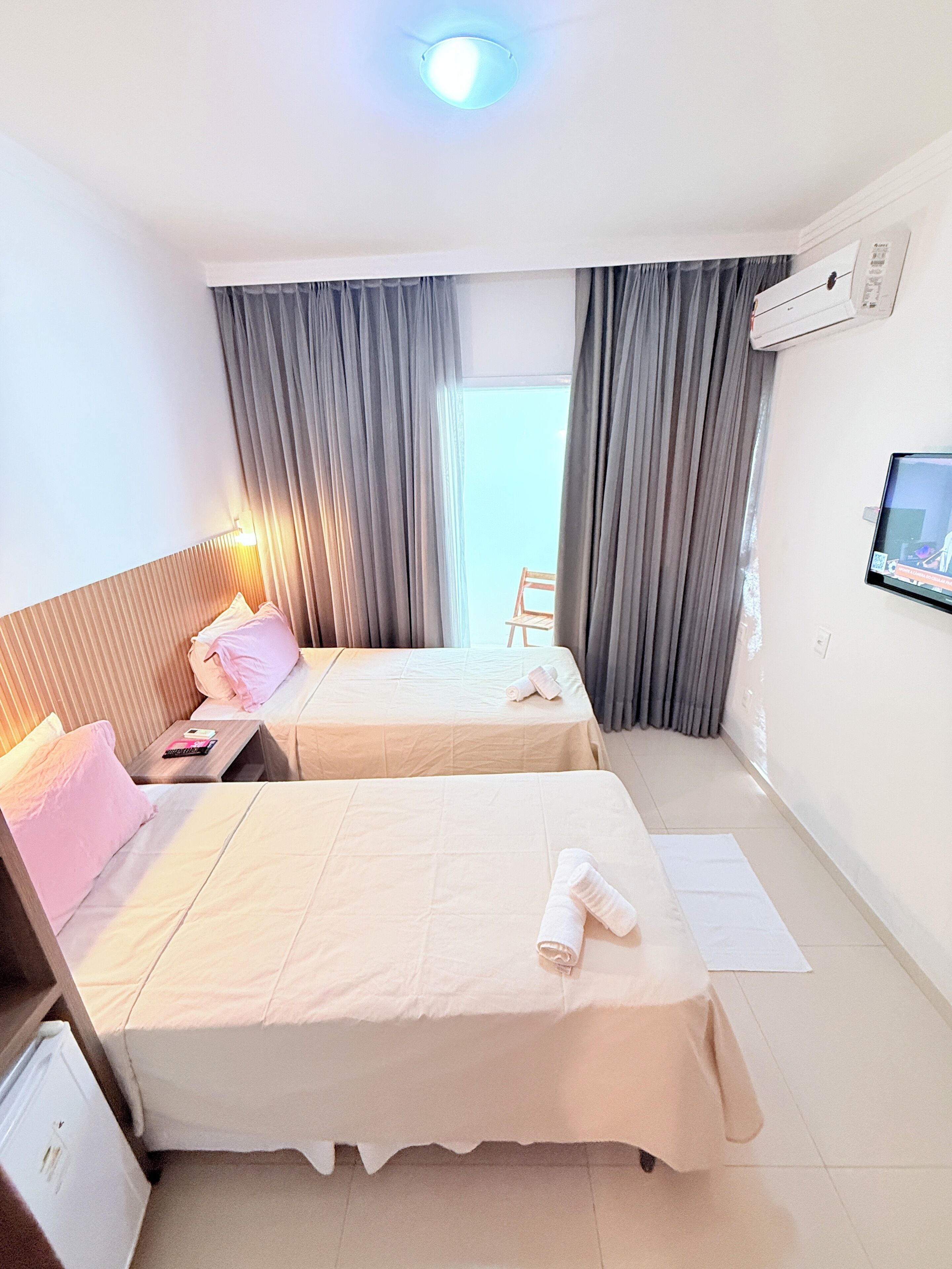A hotel room with two beds, a TV on the wall, and a window with curtains.