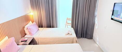 A hotel room with two beds, a TV on the wall, and a window with curtains.
