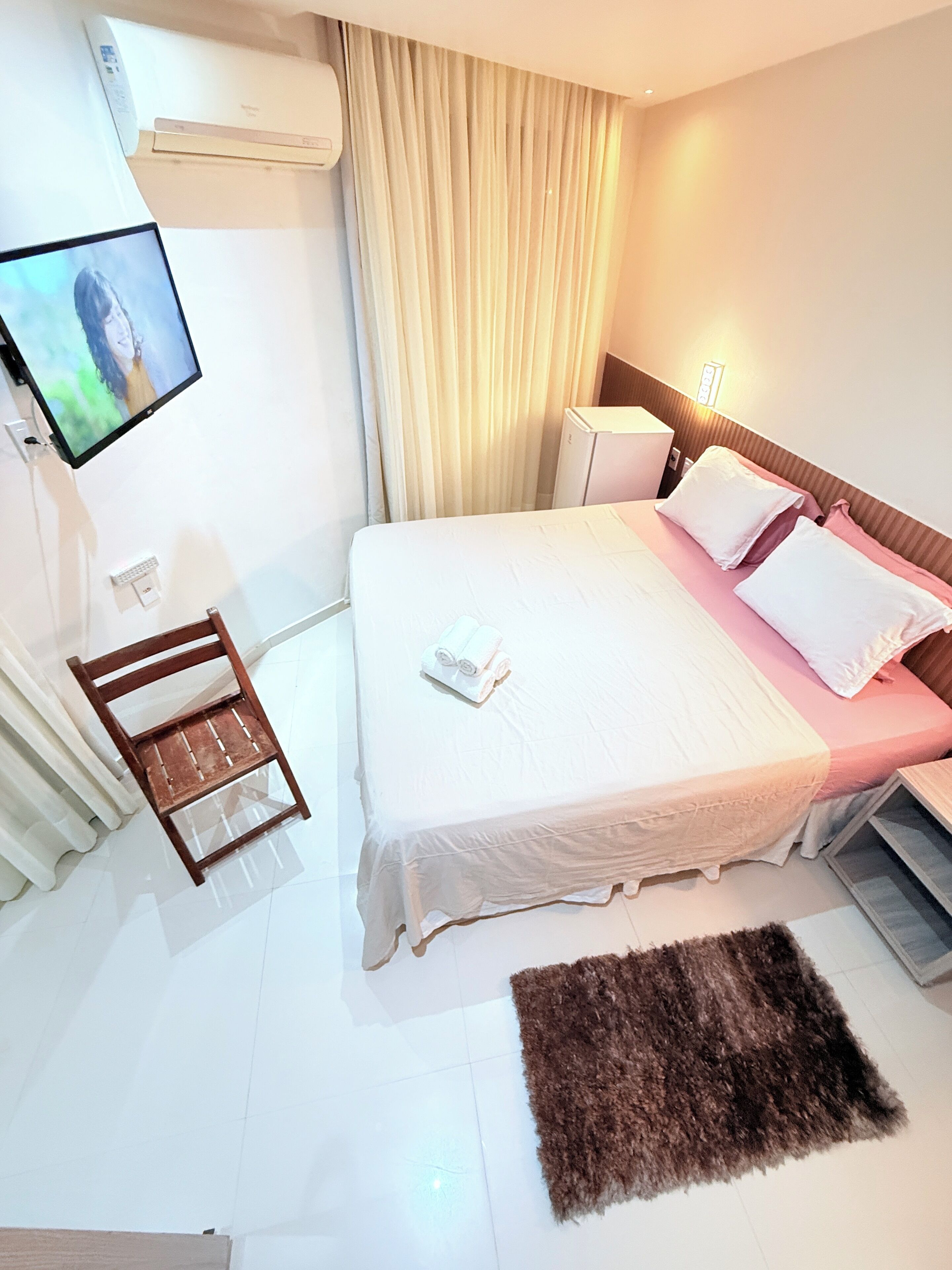 Habitación de hotel con cama, televisión montada en la pared, un pequeño escritorio, una silla, una mesita de noche y una alfombra mullida en el suelo.