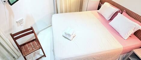 Habitación de hotel con cama, televisión montada en la pared, un pequeño escritorio, una silla, una mesita de noche y una alfombra mullida en el suelo.