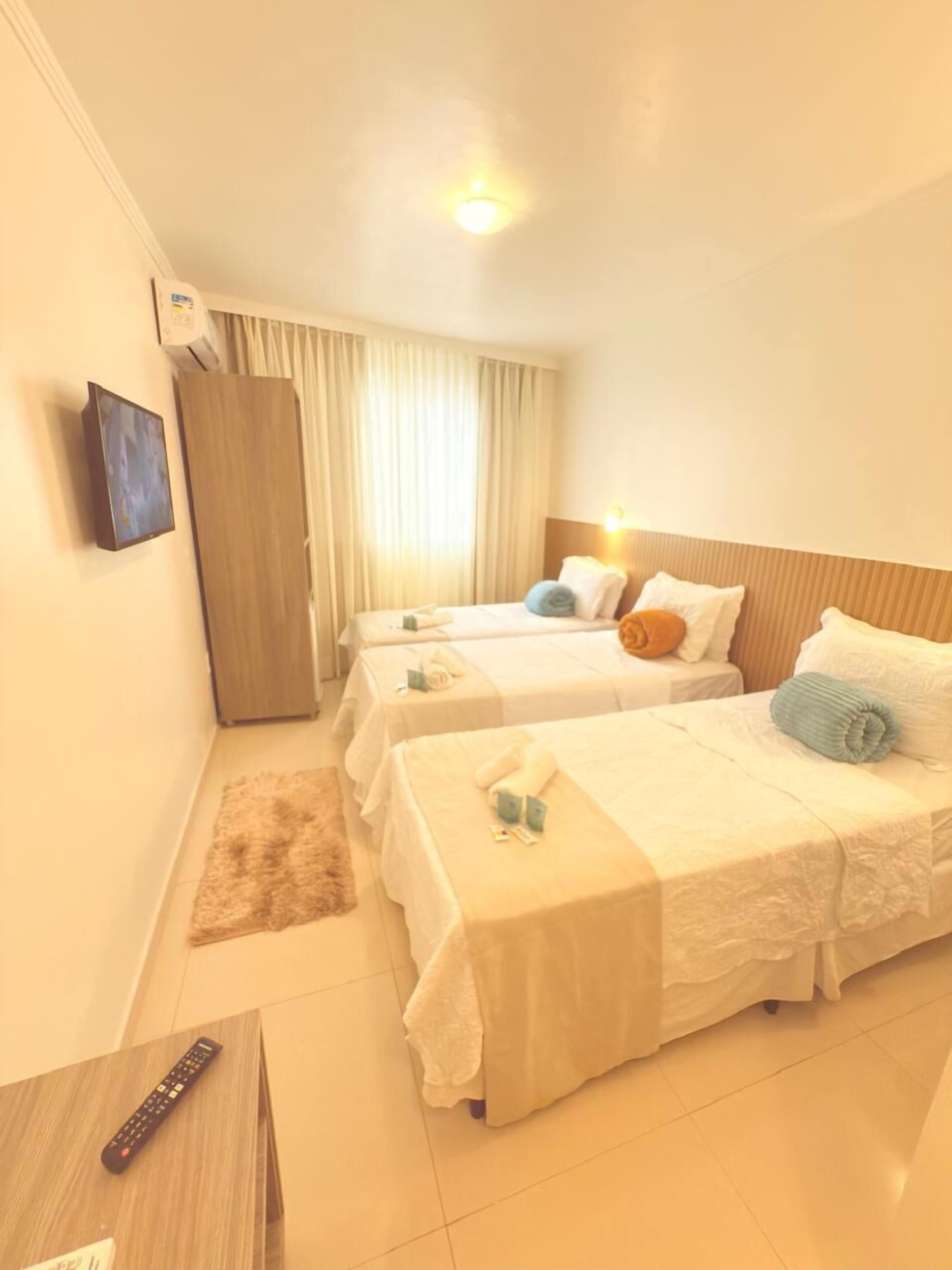 A hotel room with two beds, a wooden wardrobe, a remote control, and a small rug.