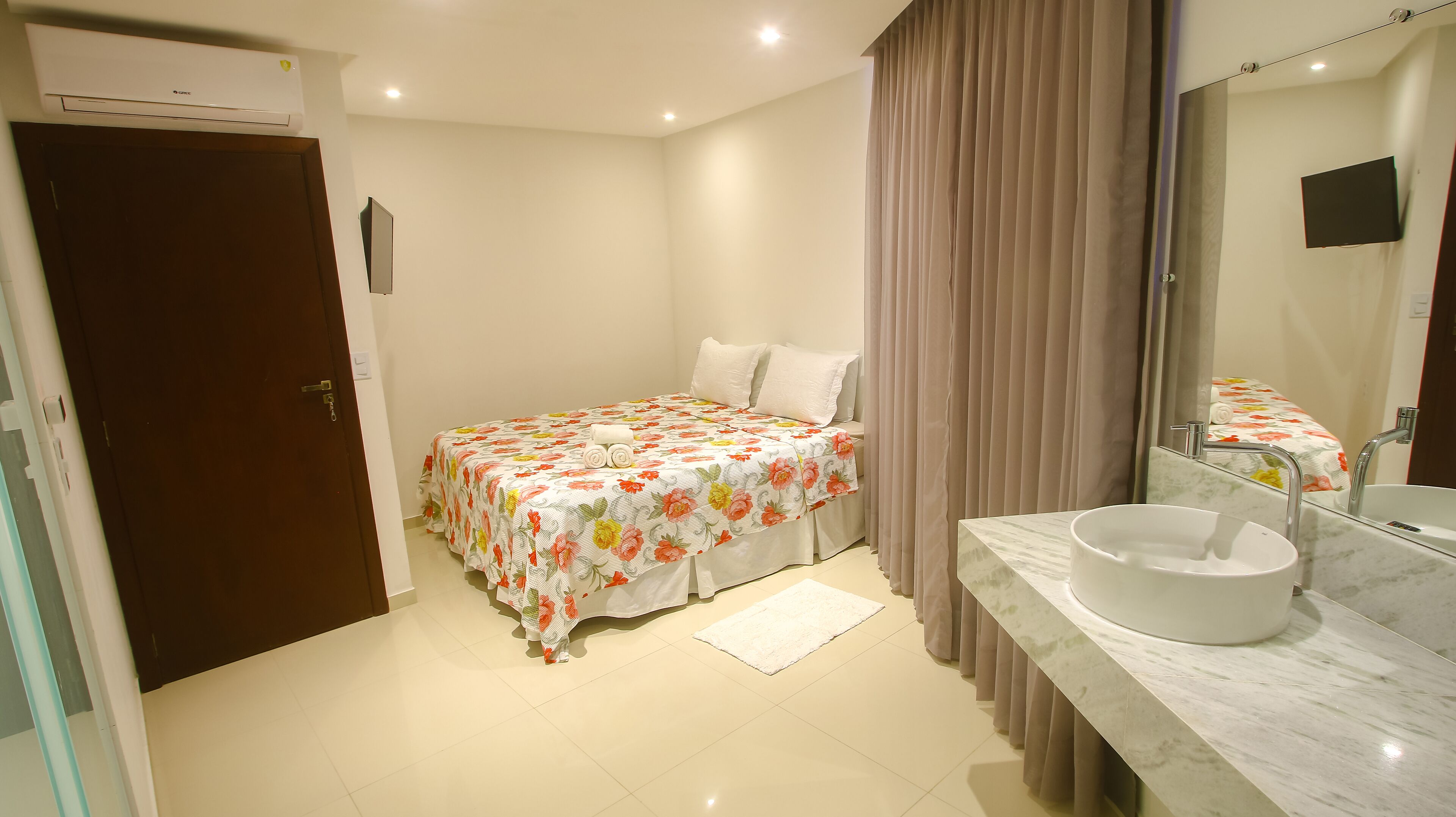 Un dormitorio con cama, un baño con lavamanos y espejo, y una puerta.