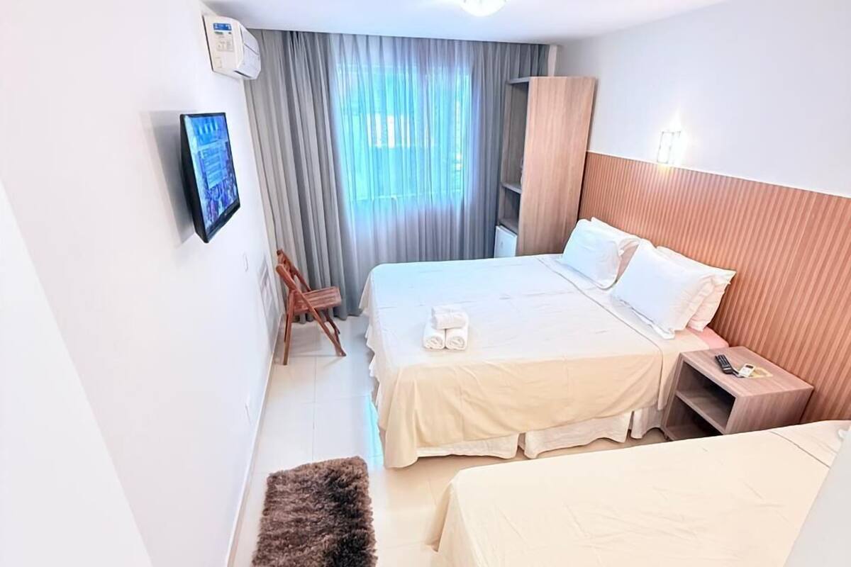 Ein Hotelzimmer mit zwei Betten, einem Fernseher, einem hölzernen Kopfteil, einem kleinen Tisch und einem Stuhl.