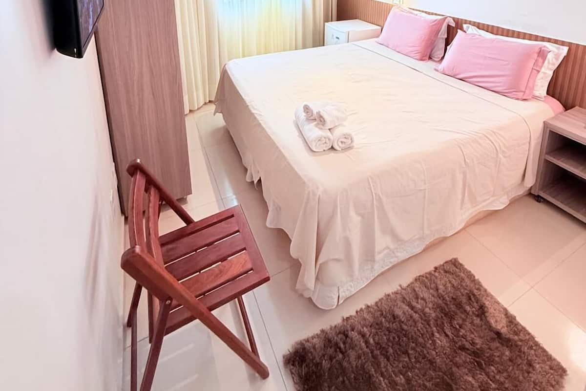 Ein Hotelzimmer mit einem Bett, einem an der Wand befestigten Fernseher, einem Holzschrank, einem Holzstuhl und einem flauschigen Teppich.