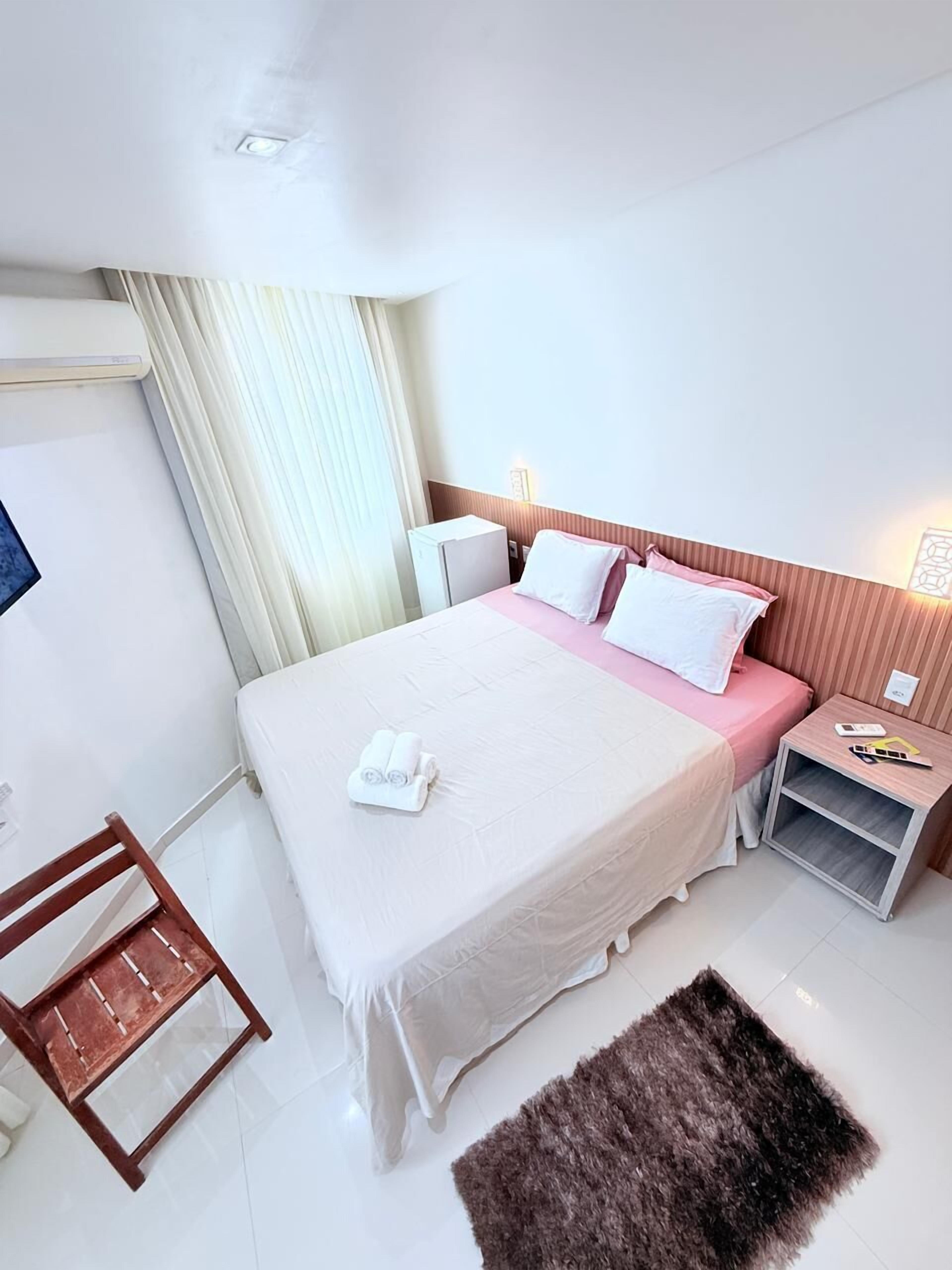 A hotel room with a large bed, a bedside table with a lamp, a small wooden chair, and a fluffy rug.