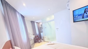 Ein modernes Hotelzimmer mit einem großen Bett, einem an der Wand befestigten Fernseher und einer Duschkabine.