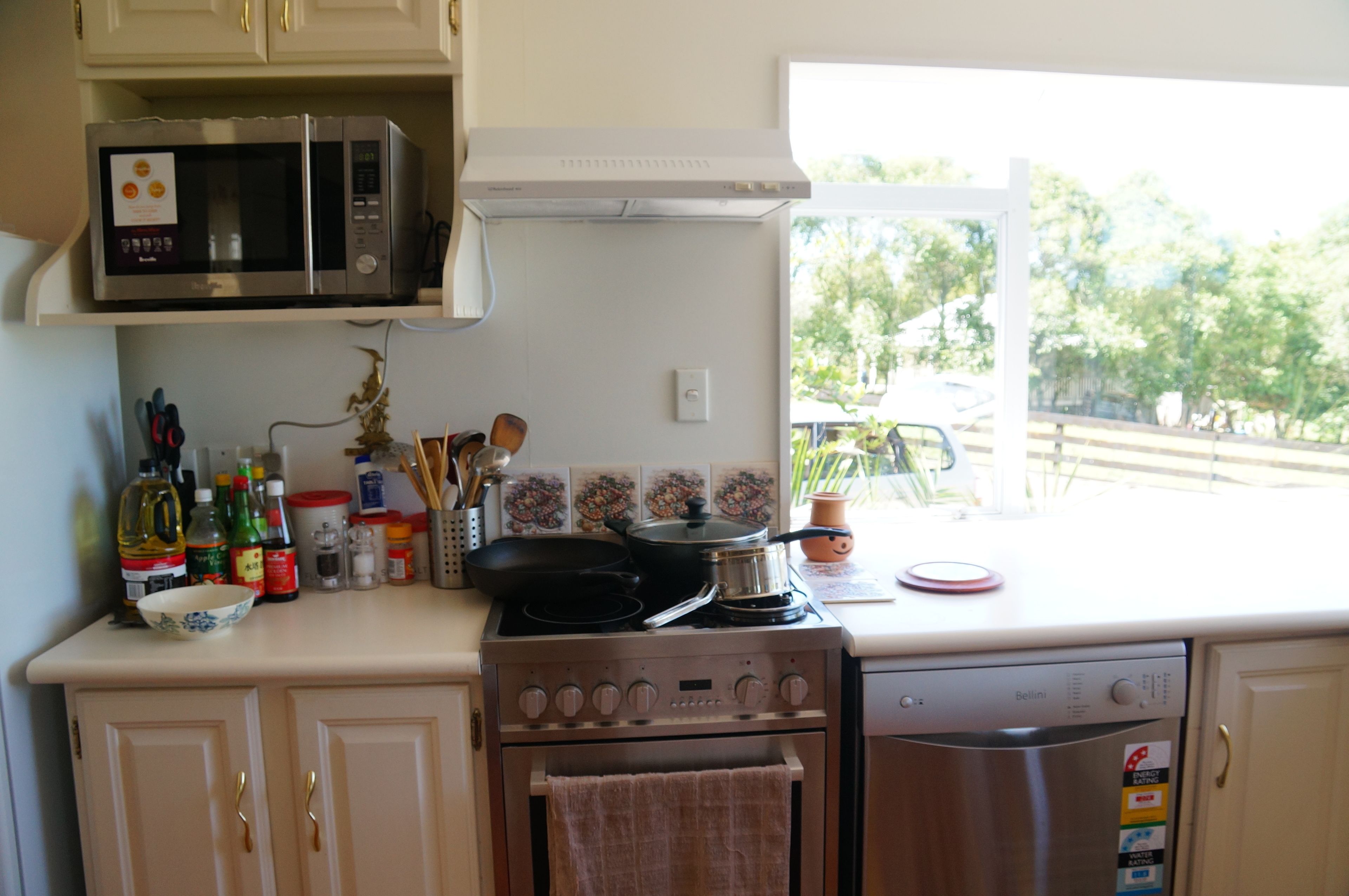 A kitchen with a microwave, stove, and dishwasher. There is a window with a view of trees and a parked car outside.