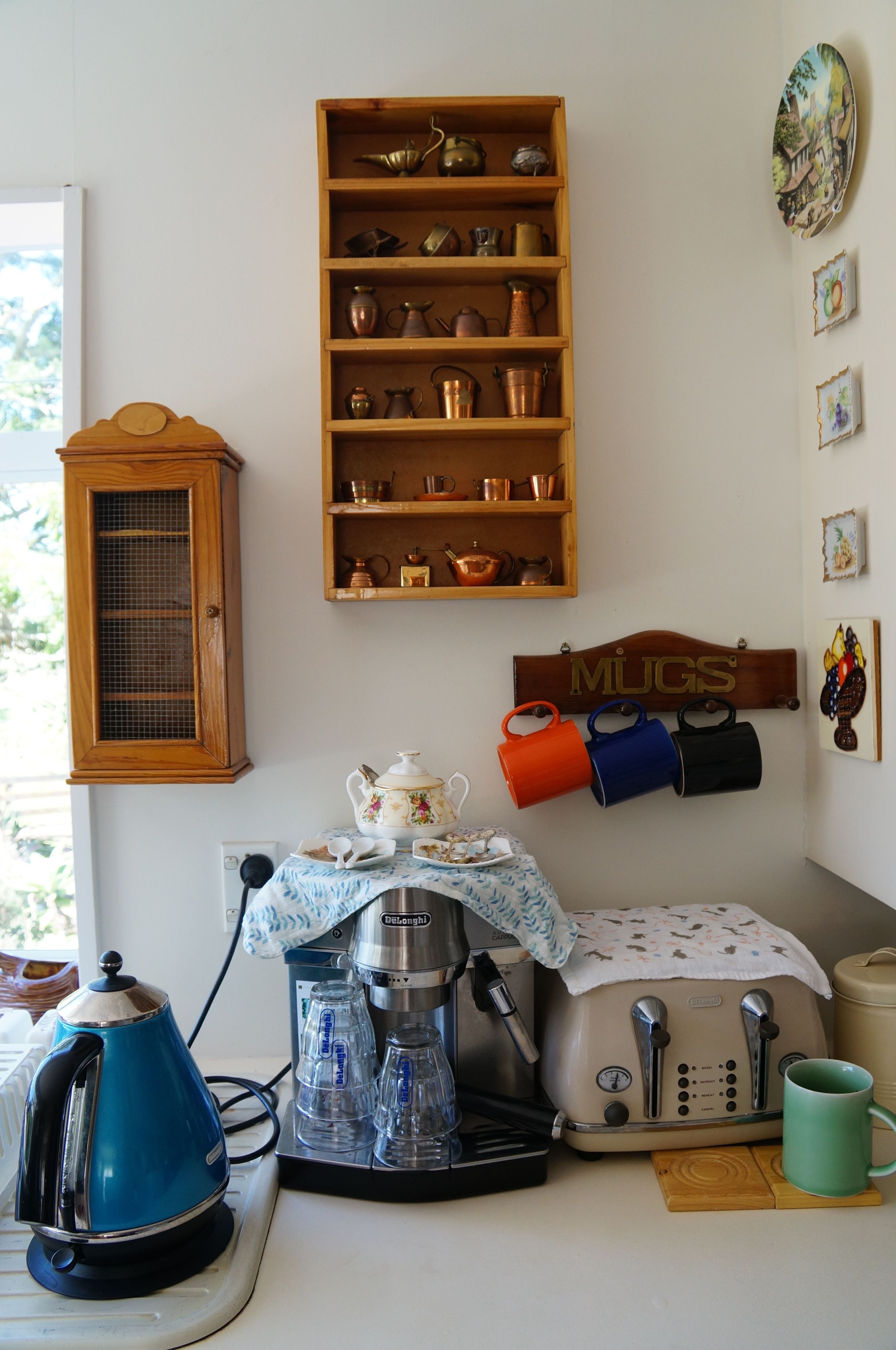 A kitchen with a coffee maker, kettle, and mug rack.