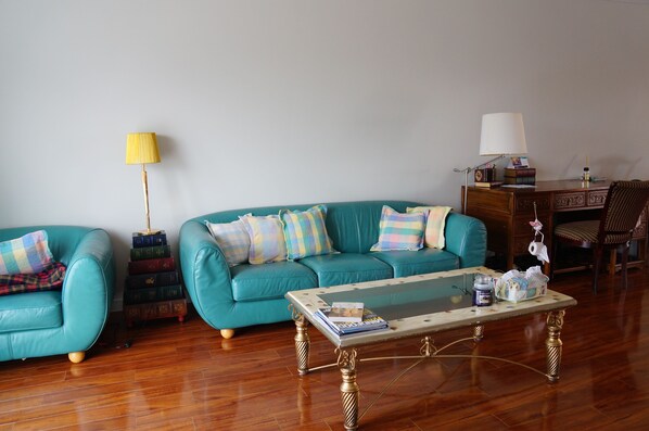 Una sala de estar con sofás color turquesa, una mesa de centro de vidrio y una mesita de noche de madera con una lámpara.