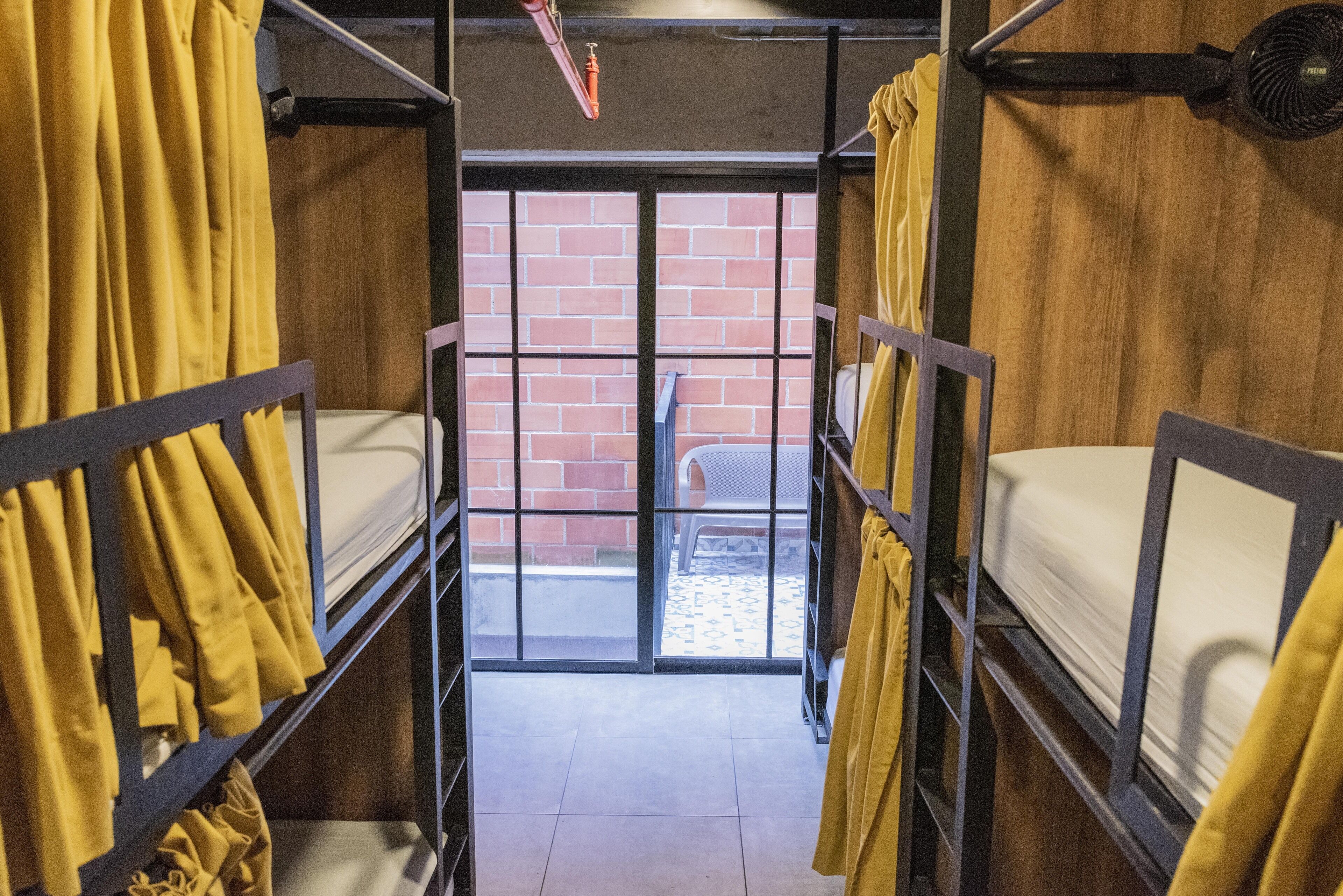 Habitación de hostal con literas, pared de ladrillo y puerta corredera de cristal que da a un espacio al aire libre.