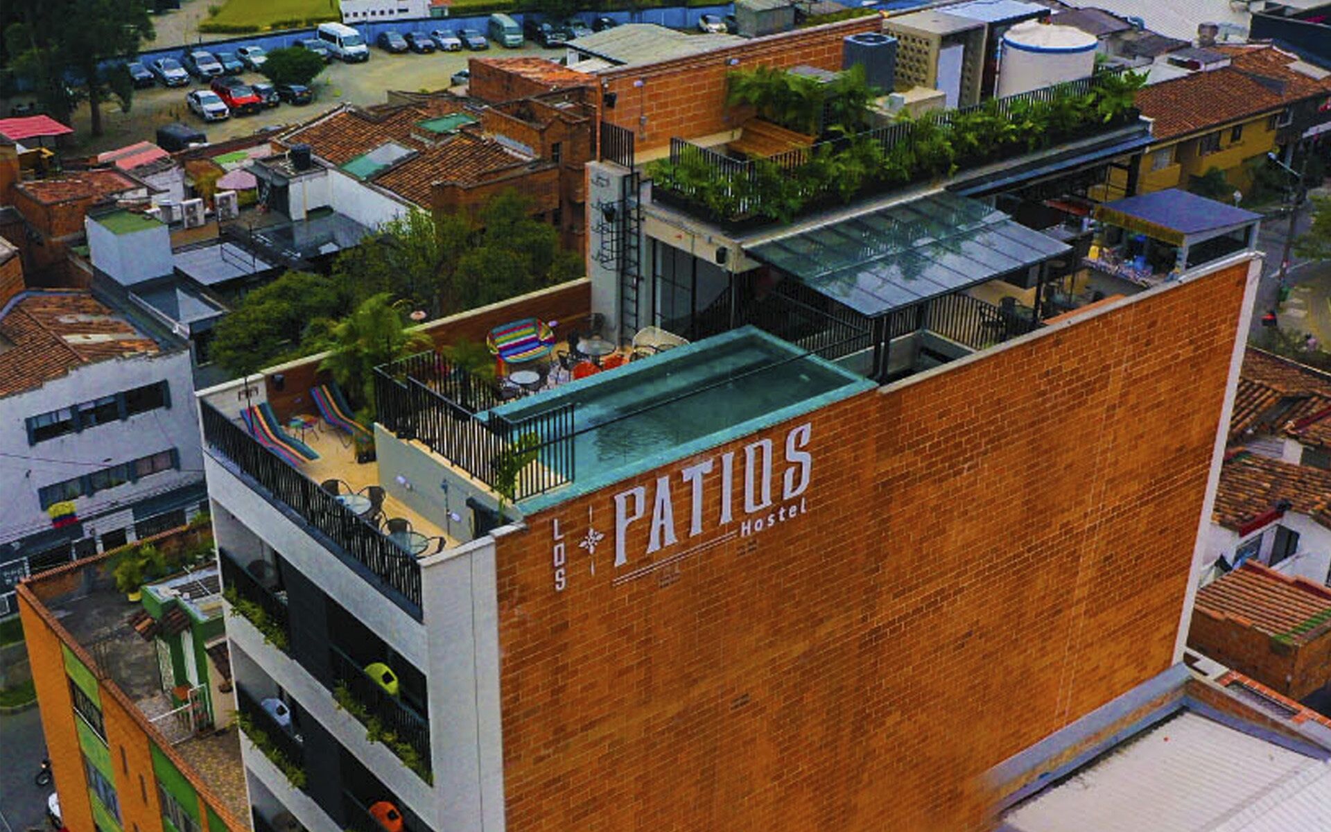 A hostel named 'Patios' with a rooftop terrace, a swimming pool, and a view of the surrounding urban area.
