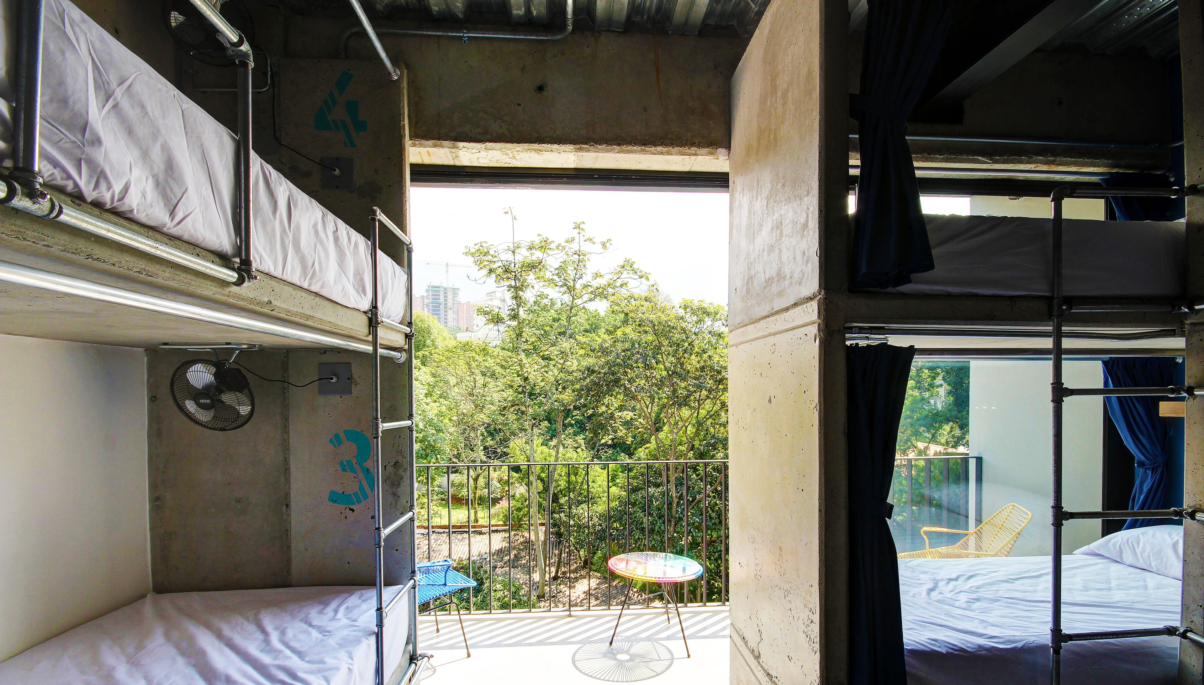 A compact train compartment with bunk beds, a small table, and a view of greenery outside.