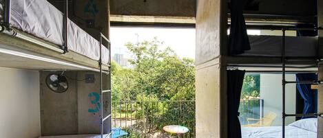 A compact train compartment with bunk beds, a small table, and a view of greenery outside.