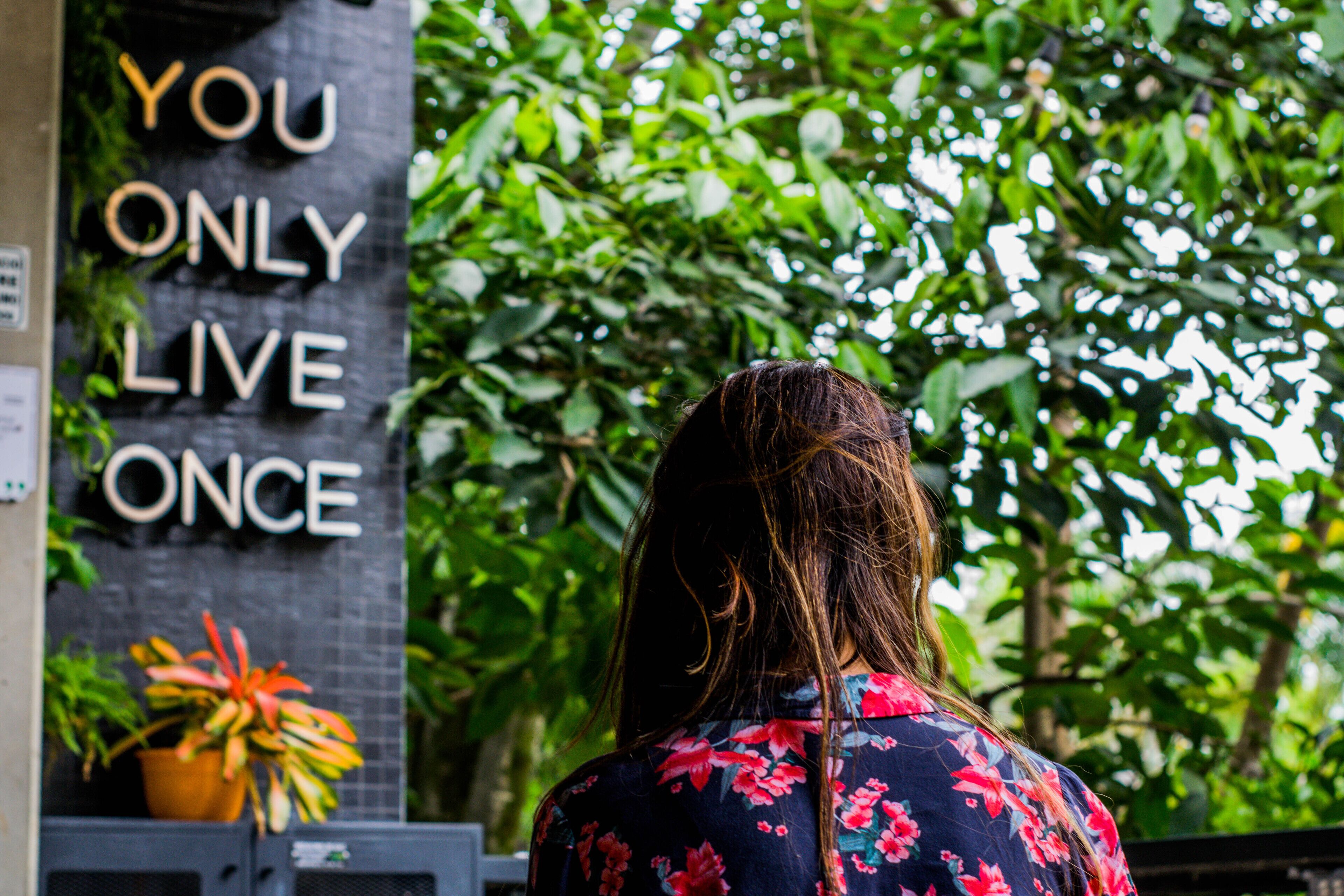 A person standing in front of a sign that reads "YOU ONLY LIVE ONCE."
