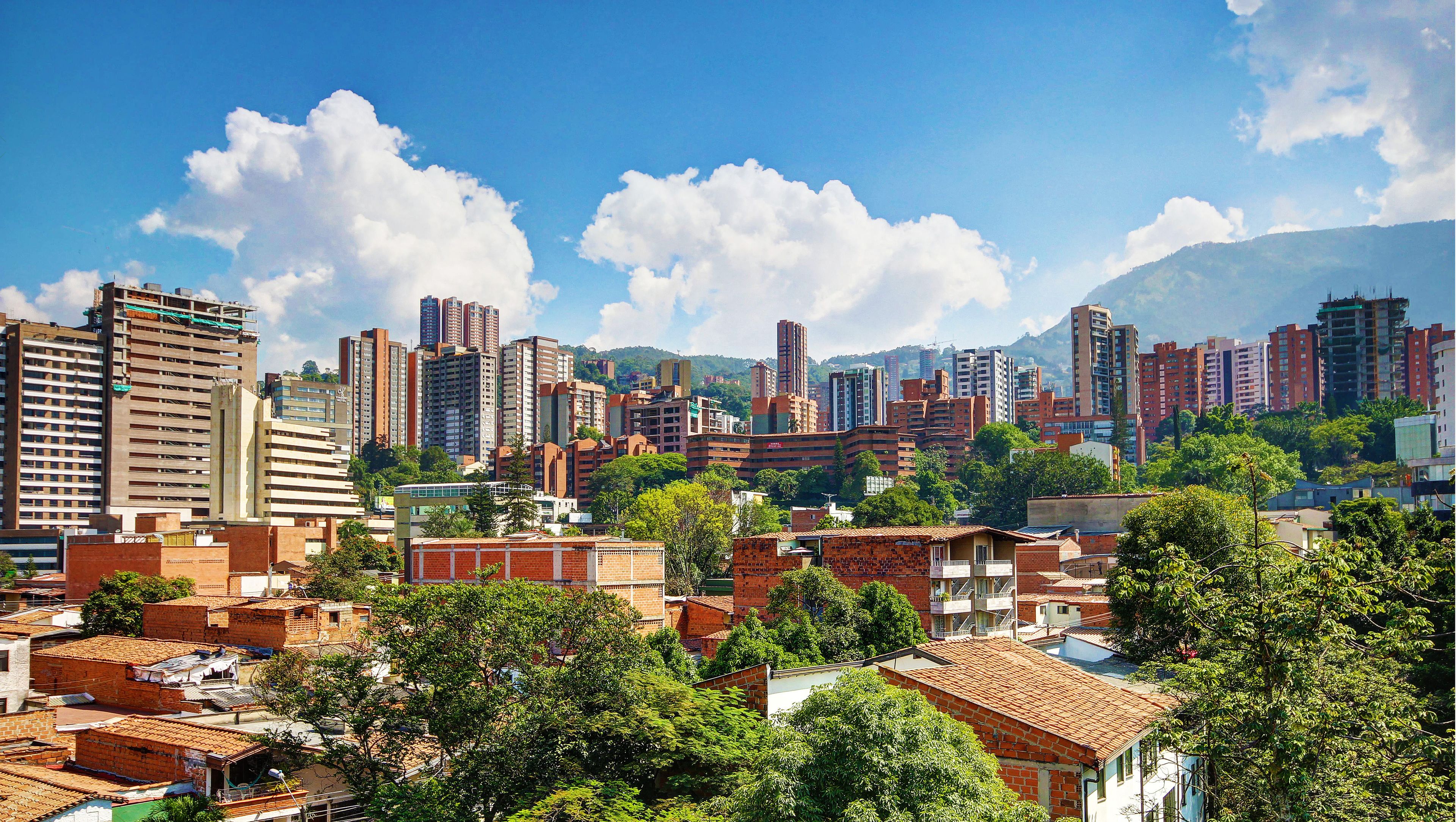 Un paysage urbain mêlant immeubles de grande hauteur et bâtiments plus bas, une végétation luxuriante et un ciel dégagé.