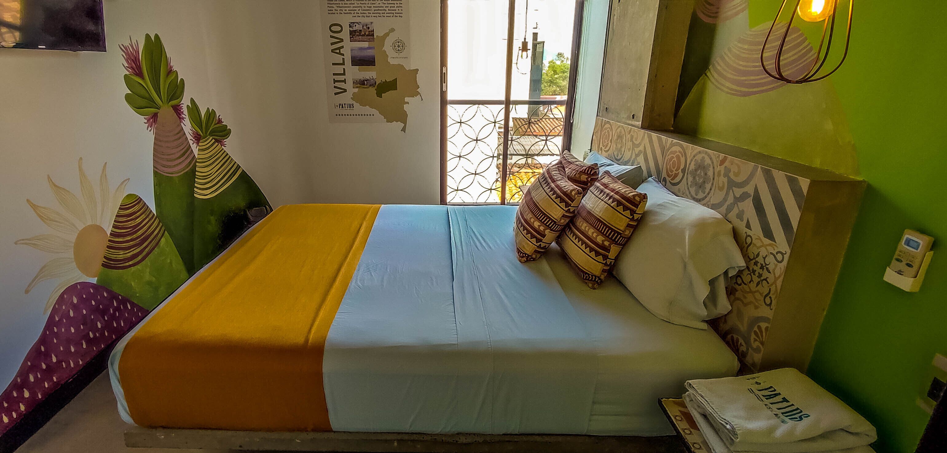 A bed with a yellow and blue bedspread, patterned pillows, and a green wall with a map and text.