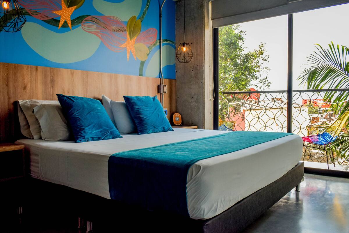 A modern bedroom with a large bed, blue and white bedding, a wooden headboard, and a colorful mural on the wall.