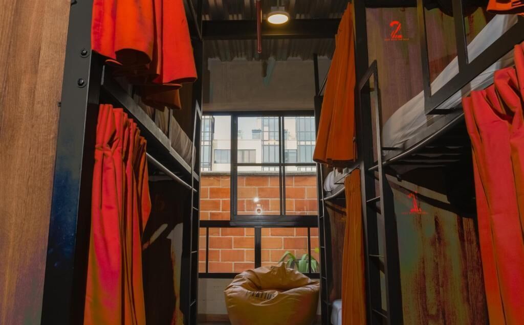 A narrow corridor with bunk beds and red curtains, leading to a window with a brick wall view.