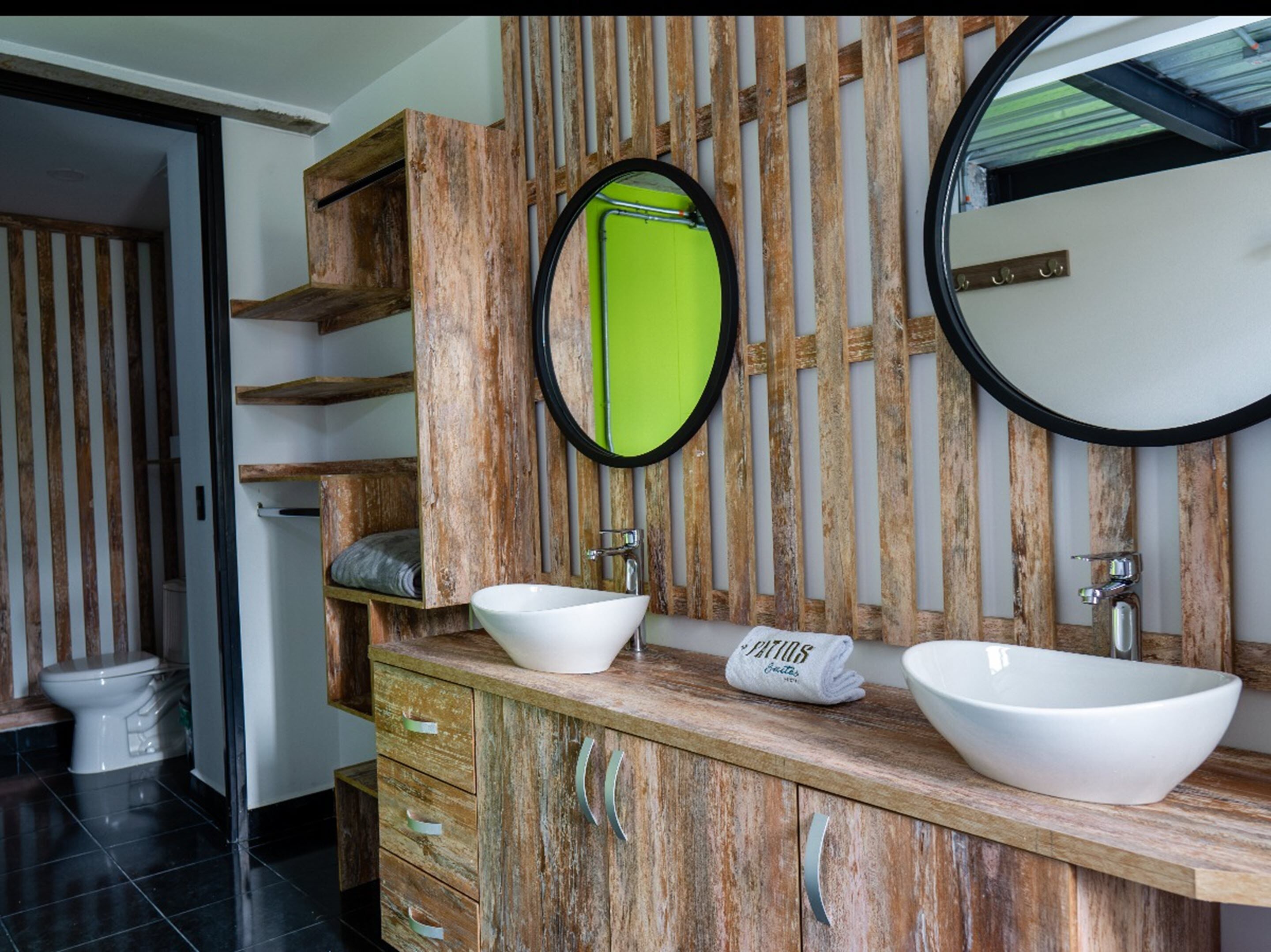 A bathroom with wooden cabinetry, two white vessel sinks, and a mirror with a green accent.