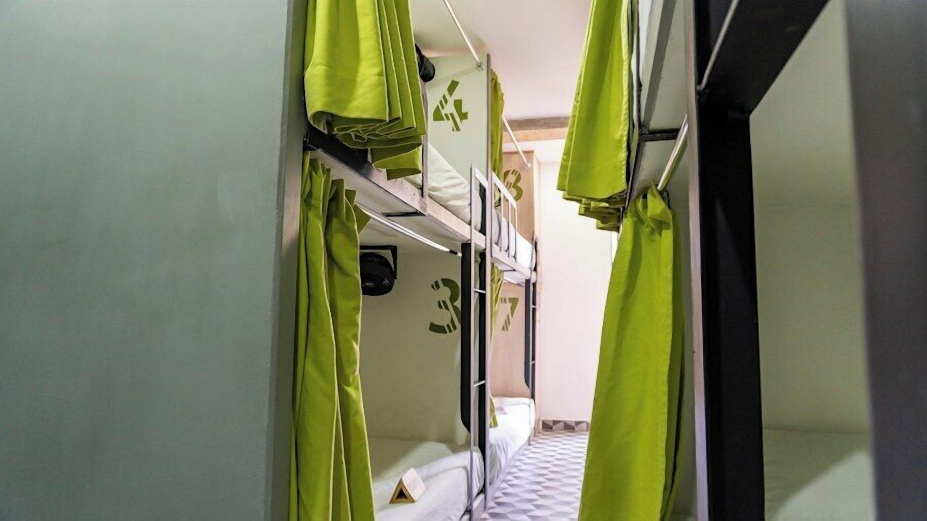 A narrow corridor with bunk beds and green curtains.