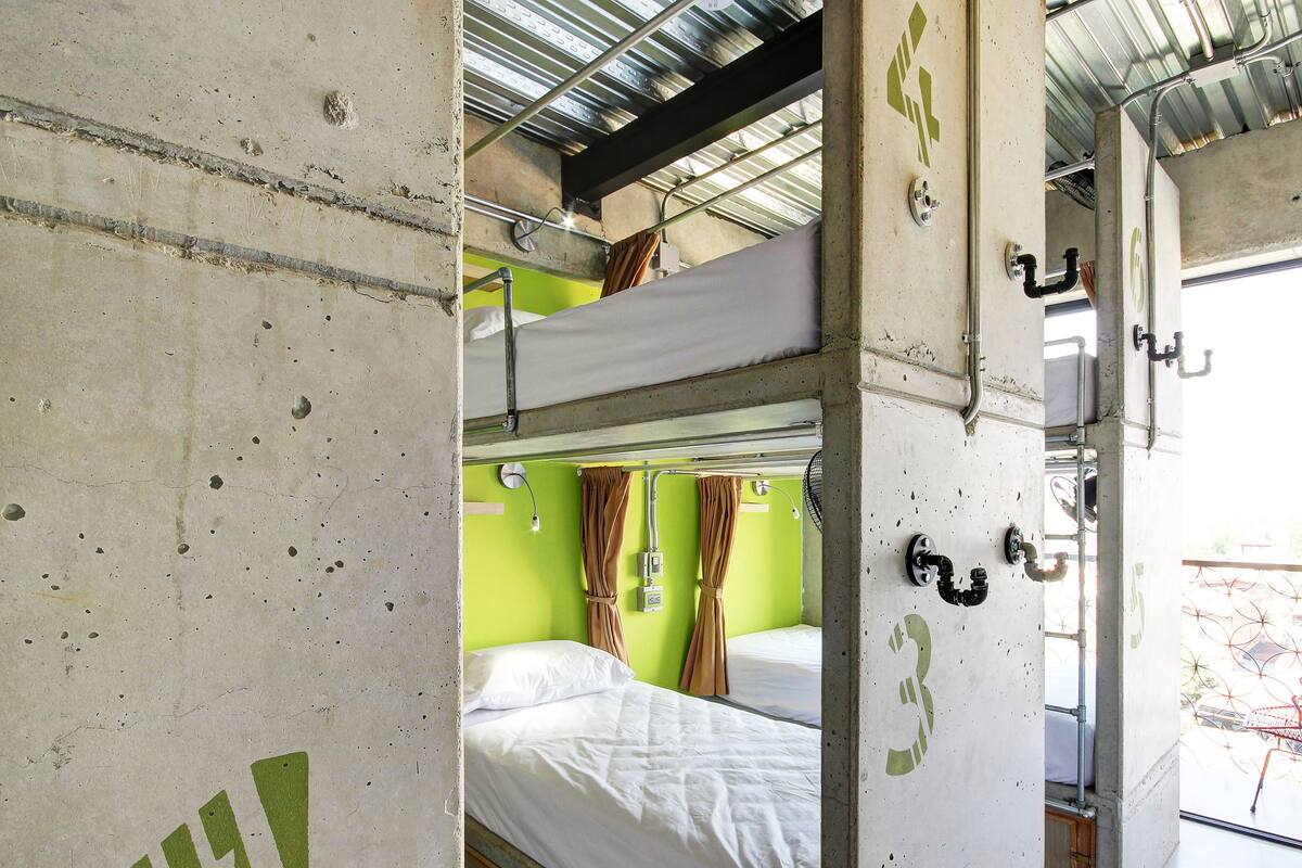 A bunk bed room with a green wall, a window with a view of a garden, and a metal ceiling.