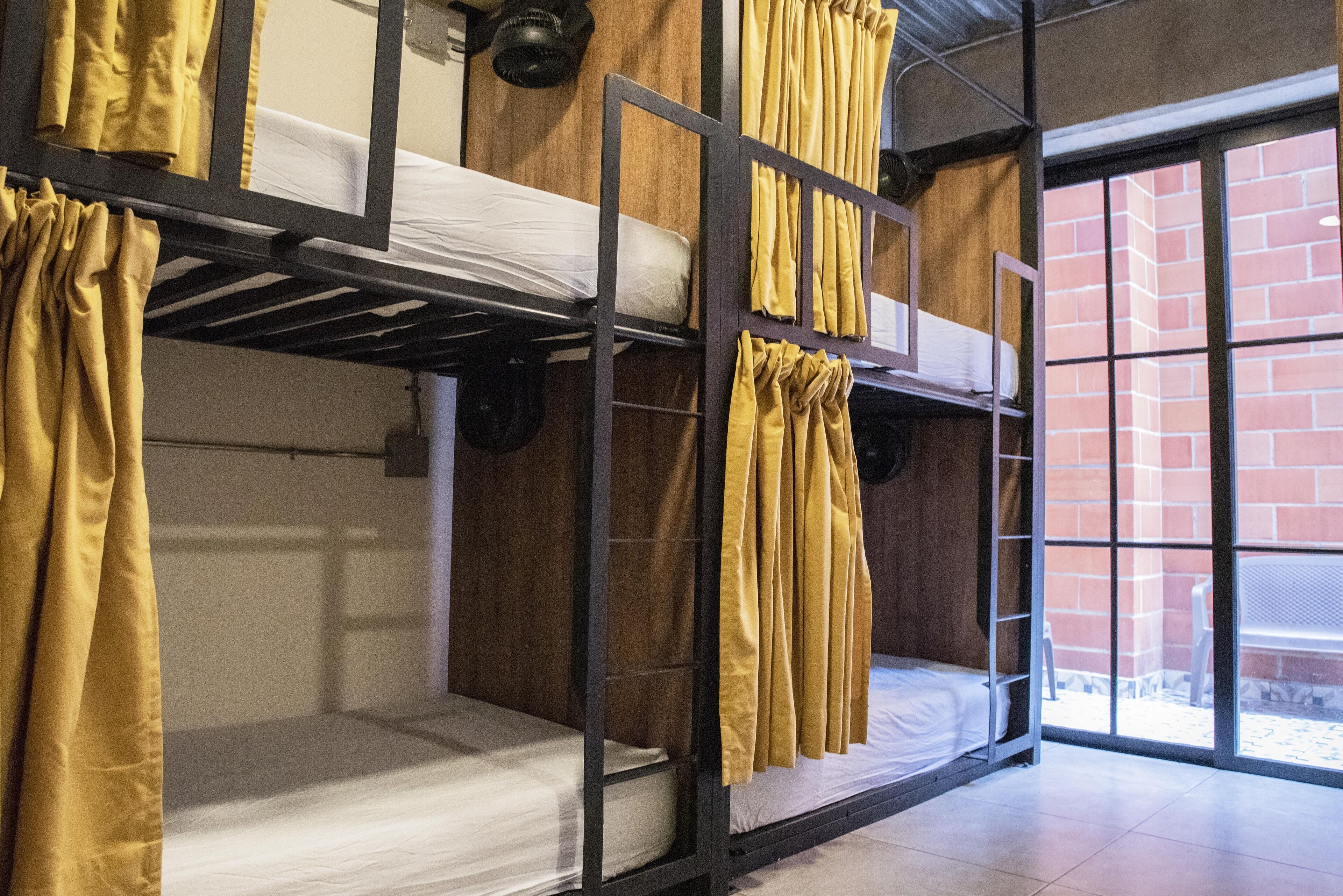 A dormitory-style room with bunk beds, wooden walls, and large windows.