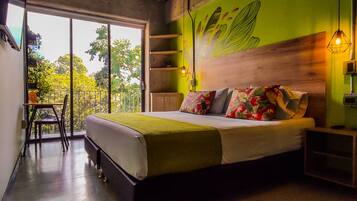 A bedroom with a bed, a nightstand, a chair, a window with a view of trees, and a green wall with a leaf design.
