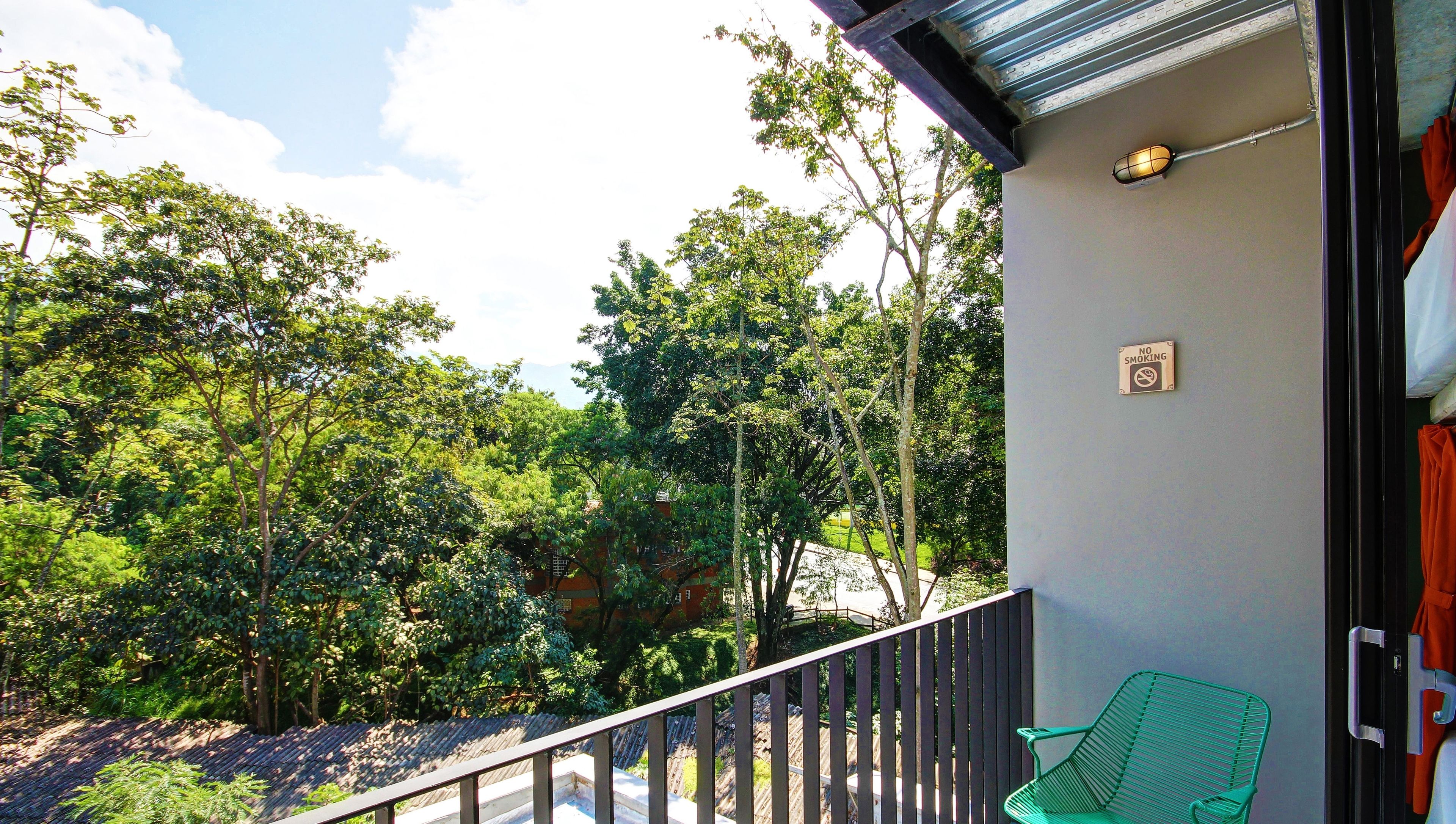 A balcony with a view of dense trees and a building in the background.