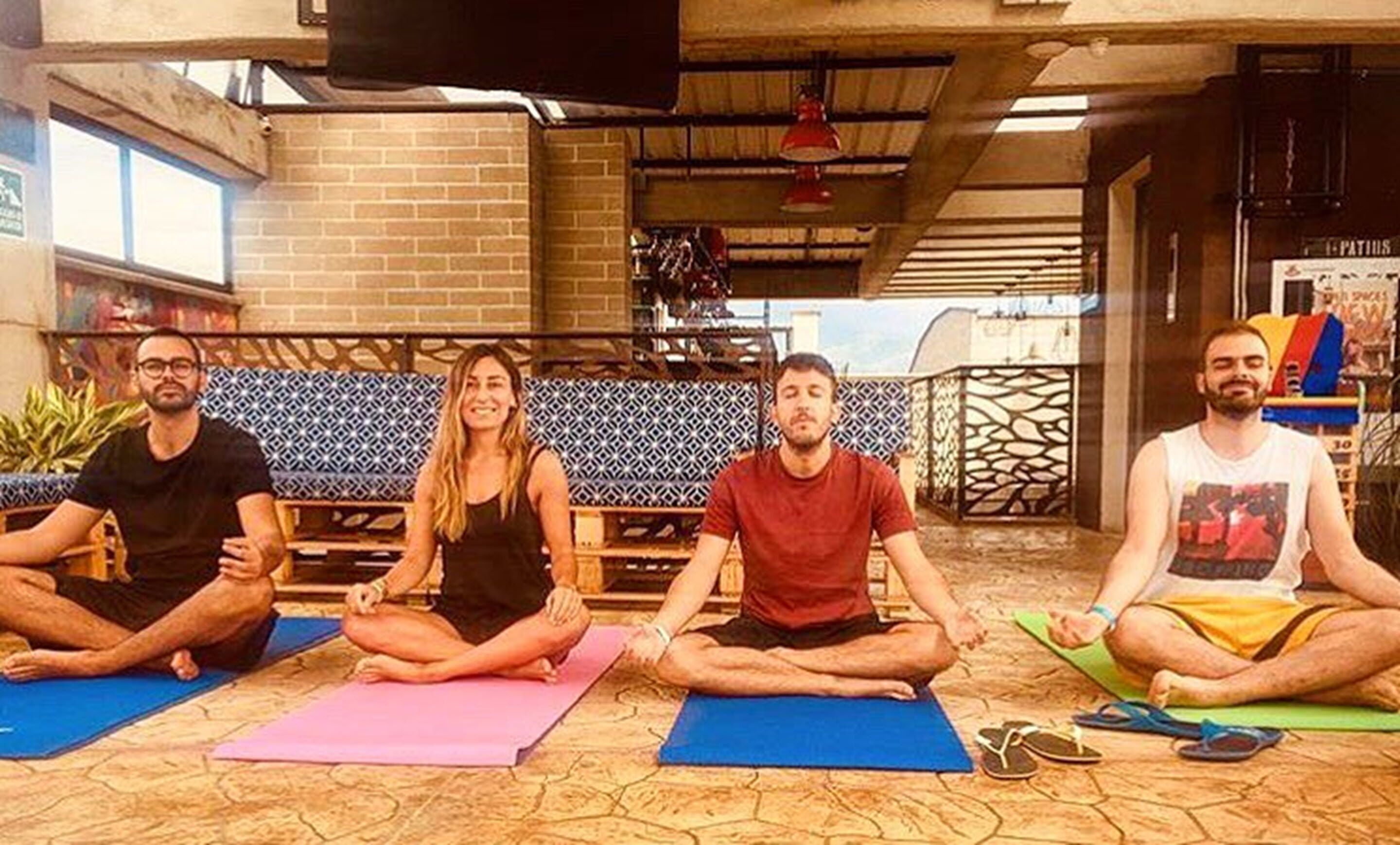 Four people seated on yoga mats in a room with brick walls and a patterned bench.
