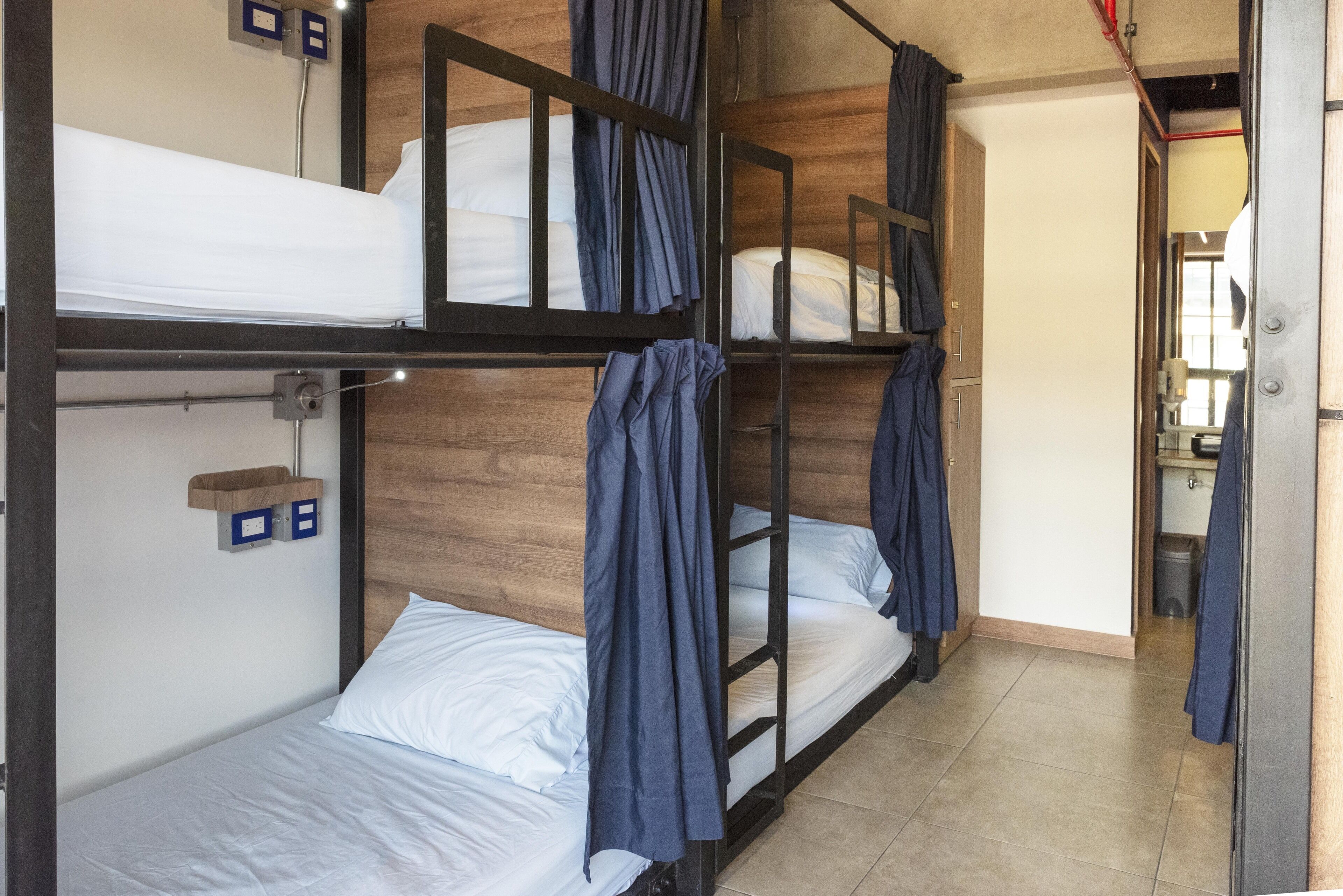 Un dormitorio con literas, una pared de madera, un pequeño estante con cajas de almacenamiento y una puerta de baño visible.