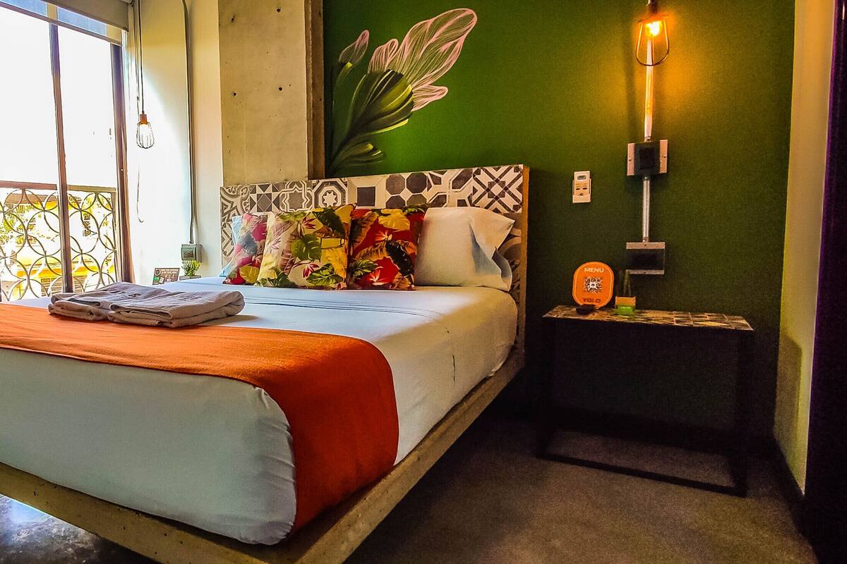 A hotel room with a bed, a nightstand, a wall map, and a green wall with a plant.
