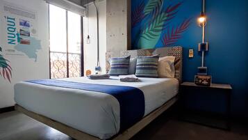 A bedroom with a bed, a wall map, a mural, and a bedside table with a lamp.