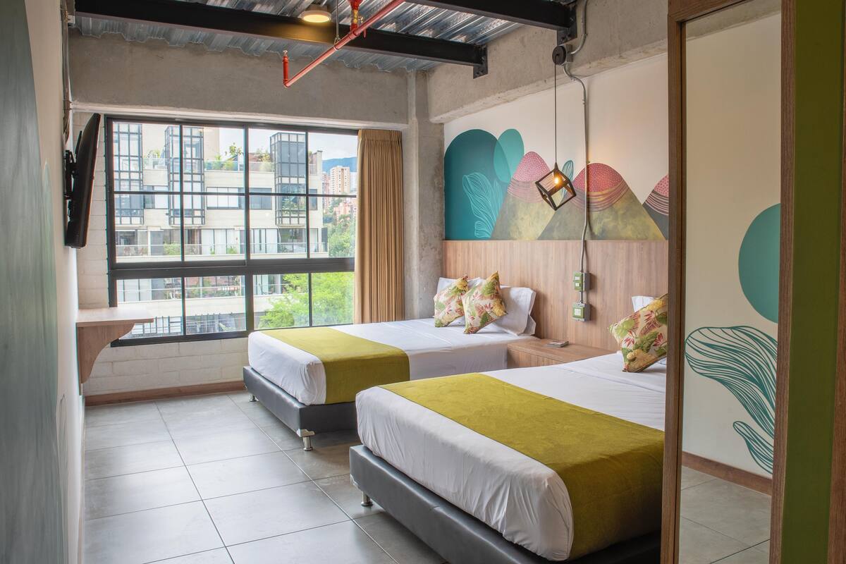 A hotel room with two beds, a large window, and a mural on the wall.