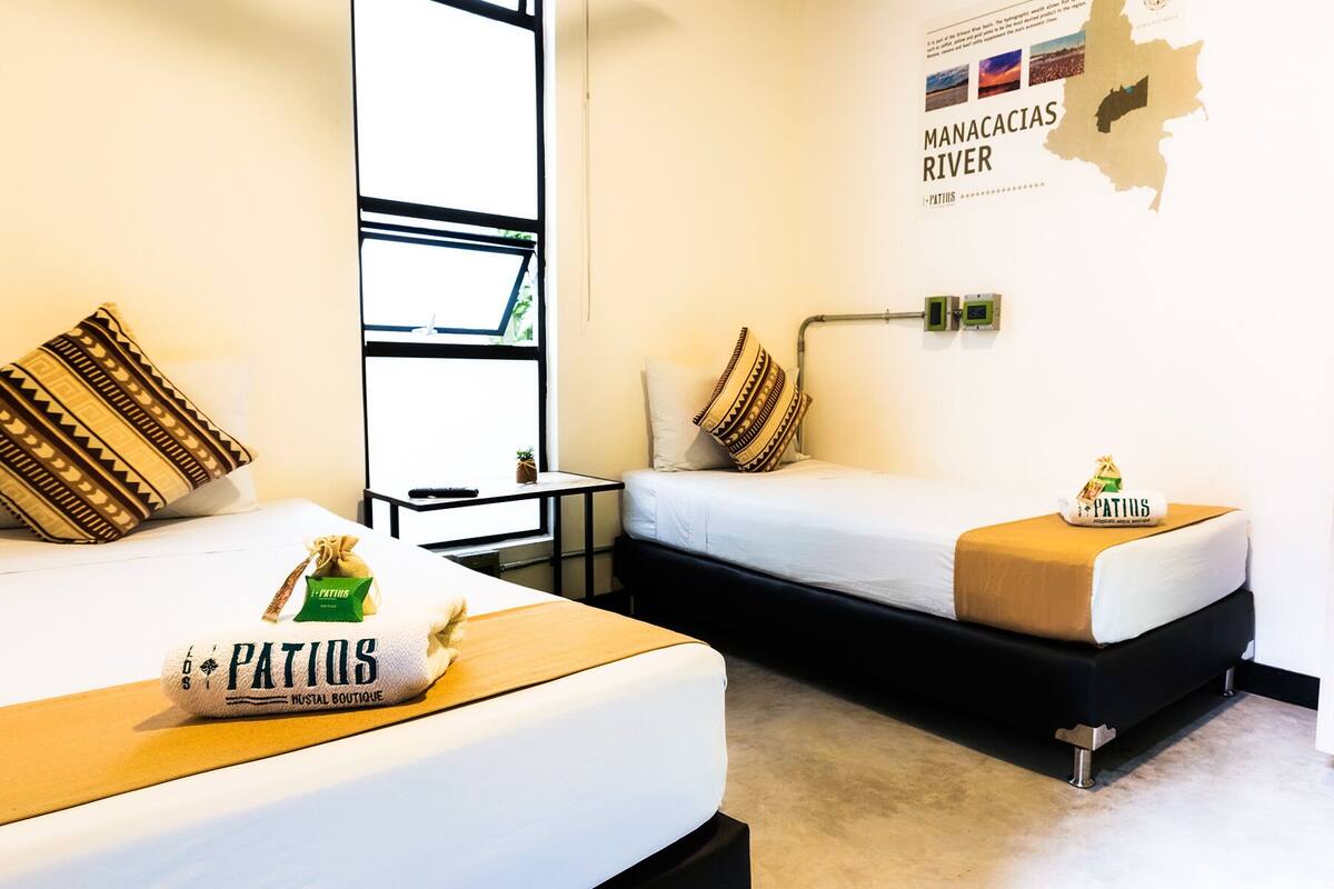 A hotel room with two beds, a map on the wall, and a small table with a towel and a bag.