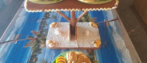 A table with a tropical beach scene design, decorated with a tree centerpiece and plates of pancakes and bread.