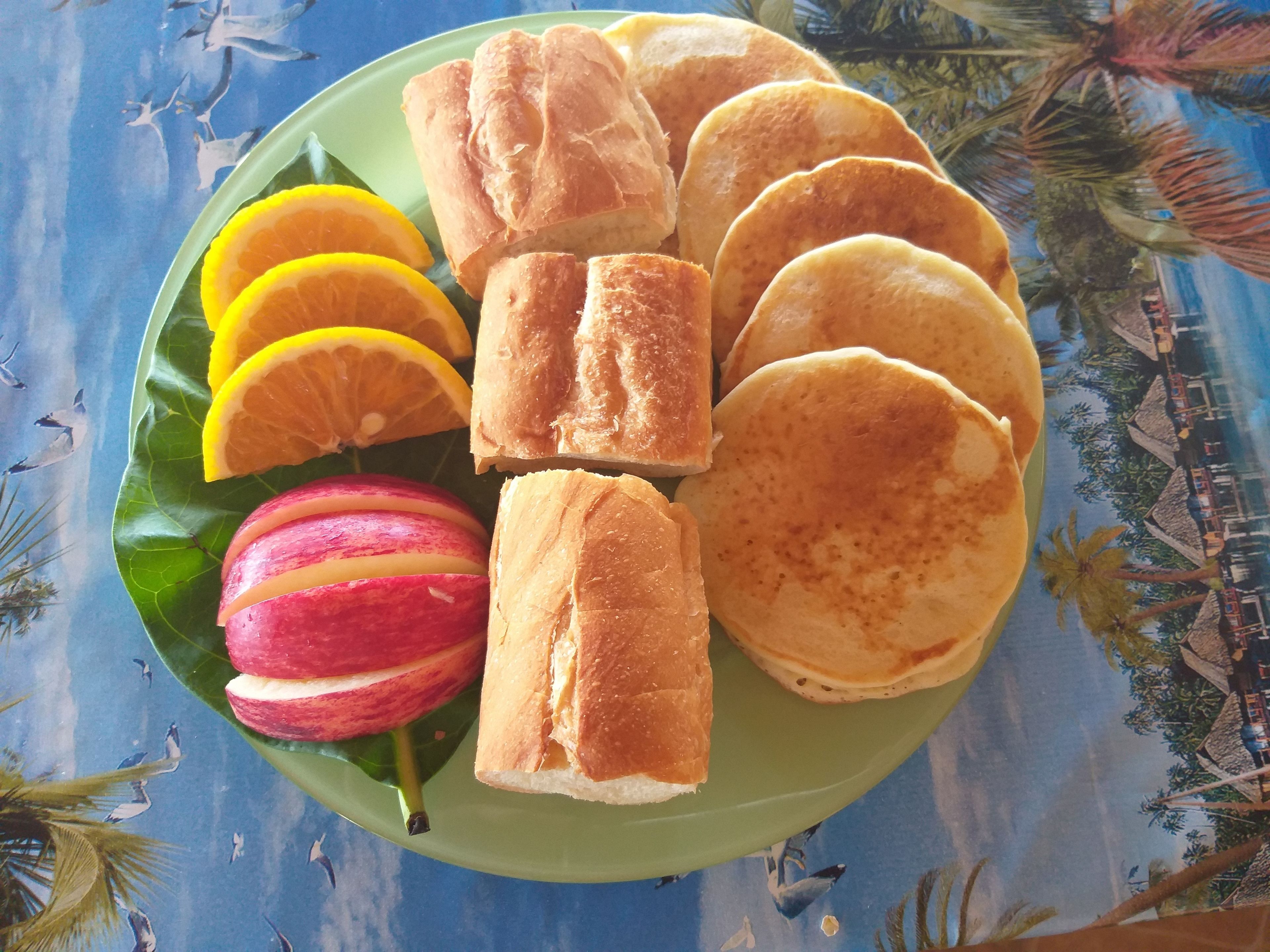 Une assiette verte contenant des crêpes, des tranches de pomme et des tranches d’orange.