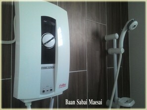 A bathroom with a white water heater, a showerhead, and a toilet.