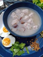 Un plato azul con sopa, albóndigas y huevos cocidos.