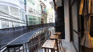 A balcony with a metal railing, wooden tables, and a view of a building with balconies and air conditioning units. - Luxury Backpackers (Hanoi)