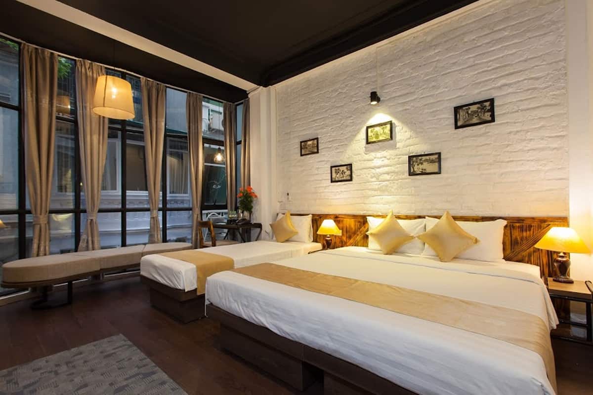 A hotel room with two beds, a bench, and a large window with curtains.