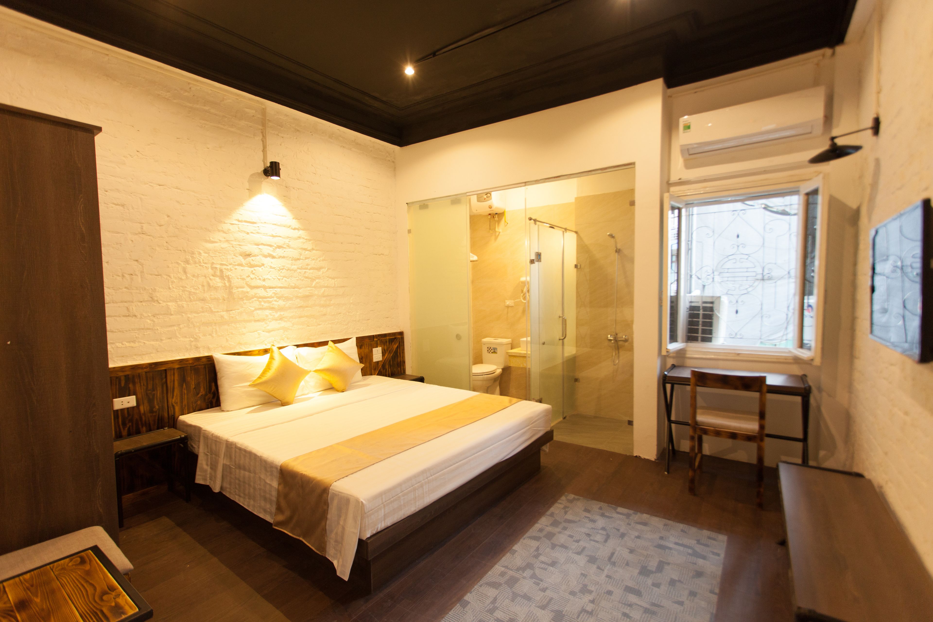 Un dormitorio con una cama grande, un banco de madera, un escritorio y una cabina de ducha de vidrio.