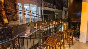 A bar area with a long counter, stools, and bottles. There are large windows and a view of the city. - Luxury Backpackers (Hanoi)