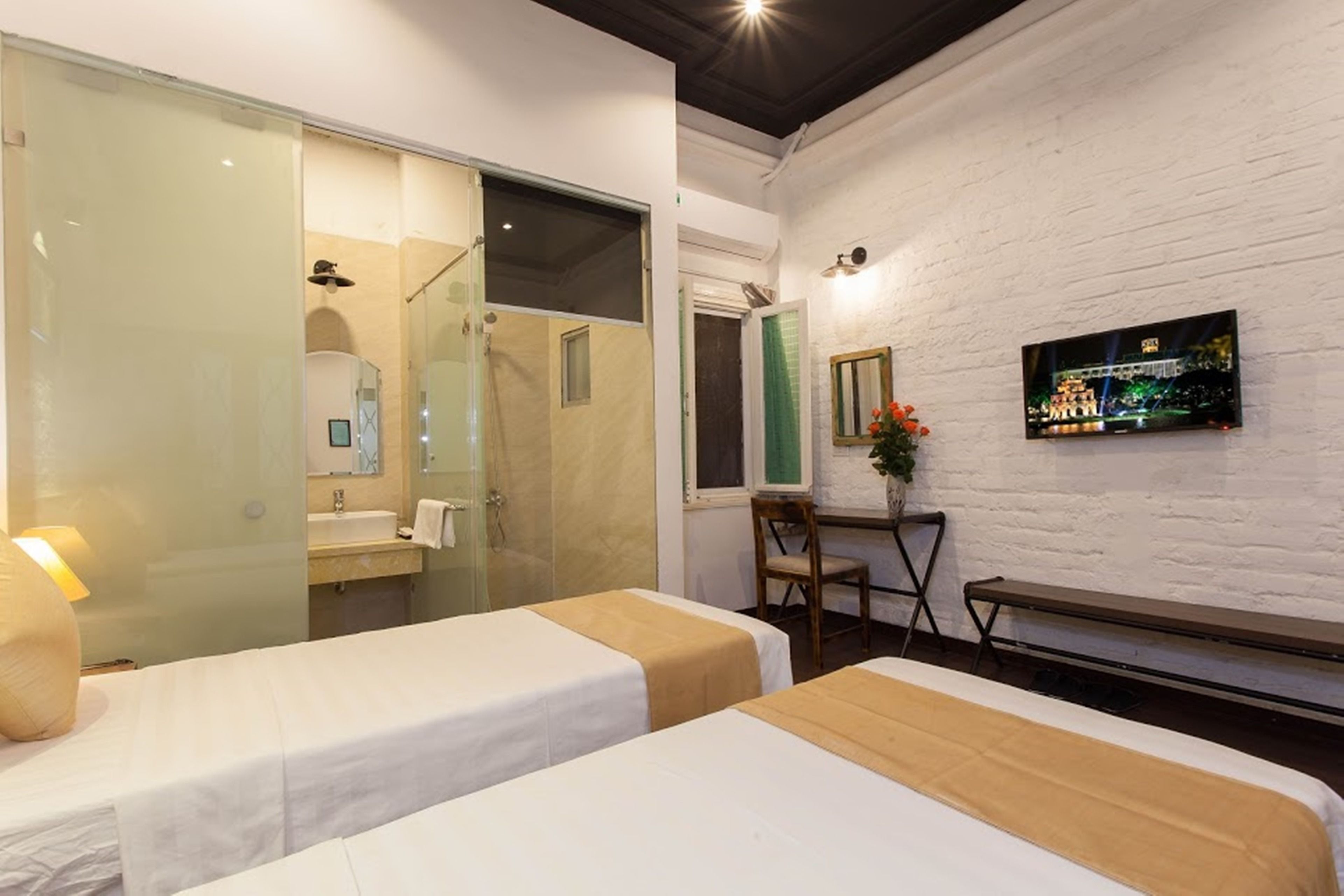 Ein Hotelzimmer mit zwei Betten, einem Badezimmer, einem Schreibtisch mit Stuhl und einem an der Wand befestigten Fernseher.