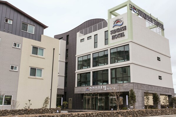 A modern hotel building with multiple floors, large windows, and a prominent sign for Sunrise Hotel.