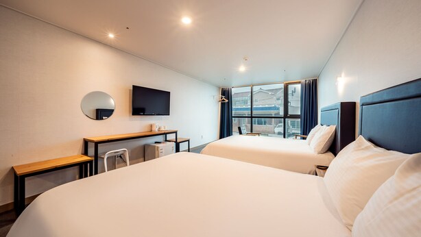 Ein Hotelzimmer mit zwei Betten, einem Schreibtisch, einem Sessel, einem Fernseher und einem Fenster mit Vorhängen.