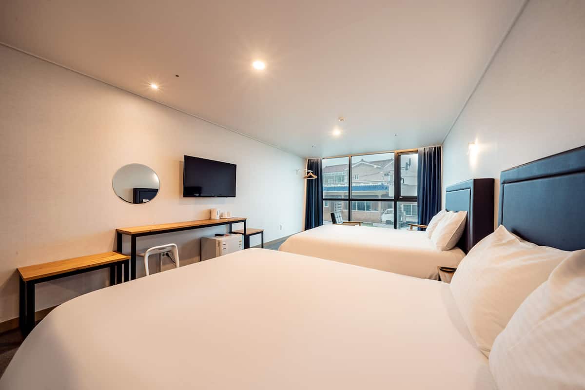 Una habitación de hotel con dos camas, un escritorio, una silla, un televisor y una ventana con cortinas.